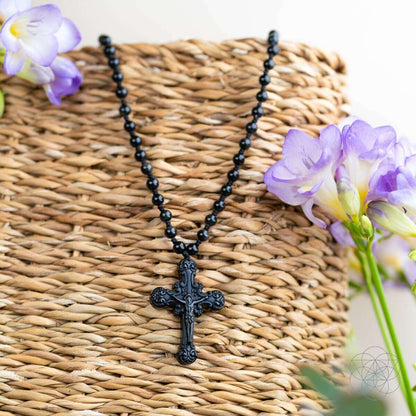 Black beaded cross pendant necklace with ornate crucifix pendant on woven background
