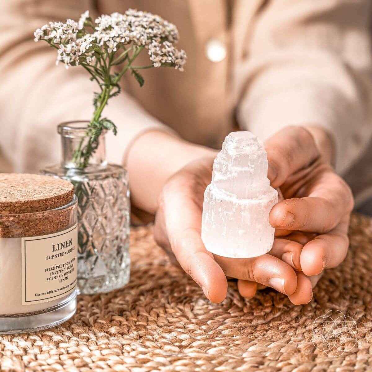 Selenite cleansing lamp crystal held in hands over woven fabric