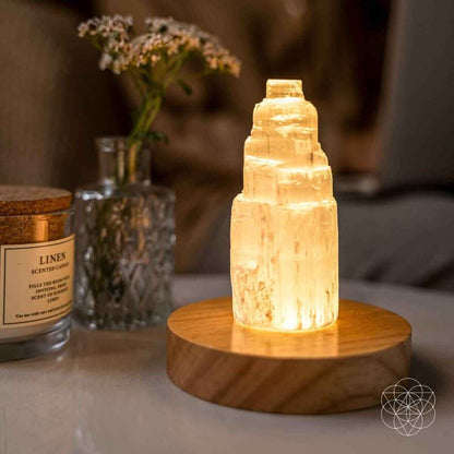 Selenite cleansing lamp with glowing amber crystal on round wooden base