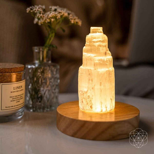 Selenite cleansing lamp with glowing amber crystal on round wooden base