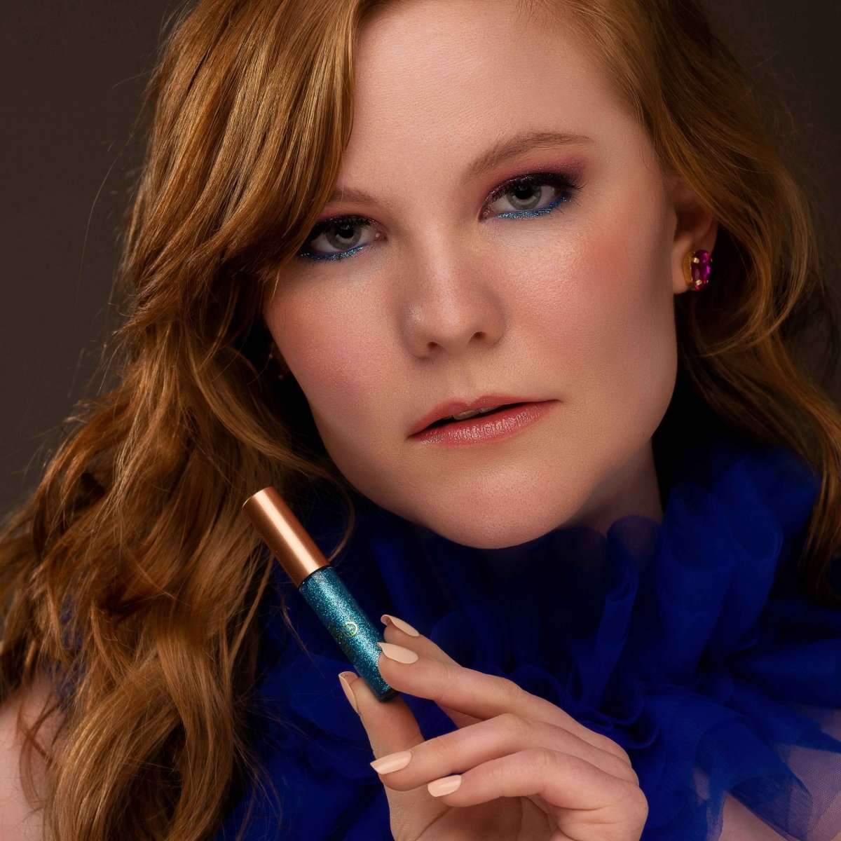 Blue glitter eyeliner on upper lash line, applicator wand held near the eye