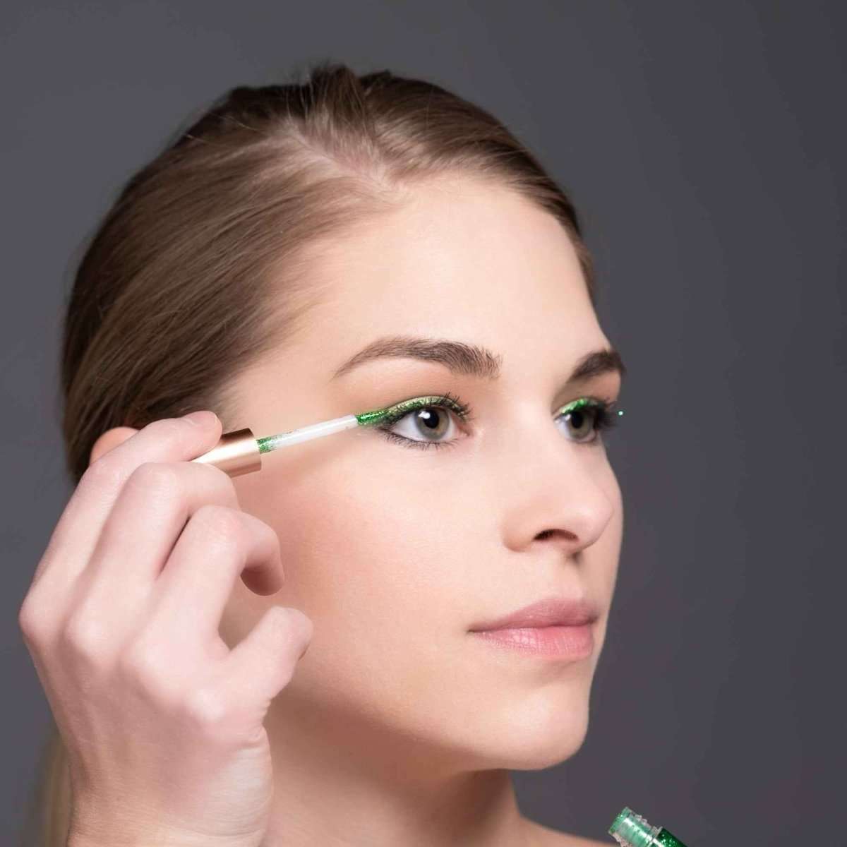 Green glitter eyeliner on eyelid, applicator wand held near the eye