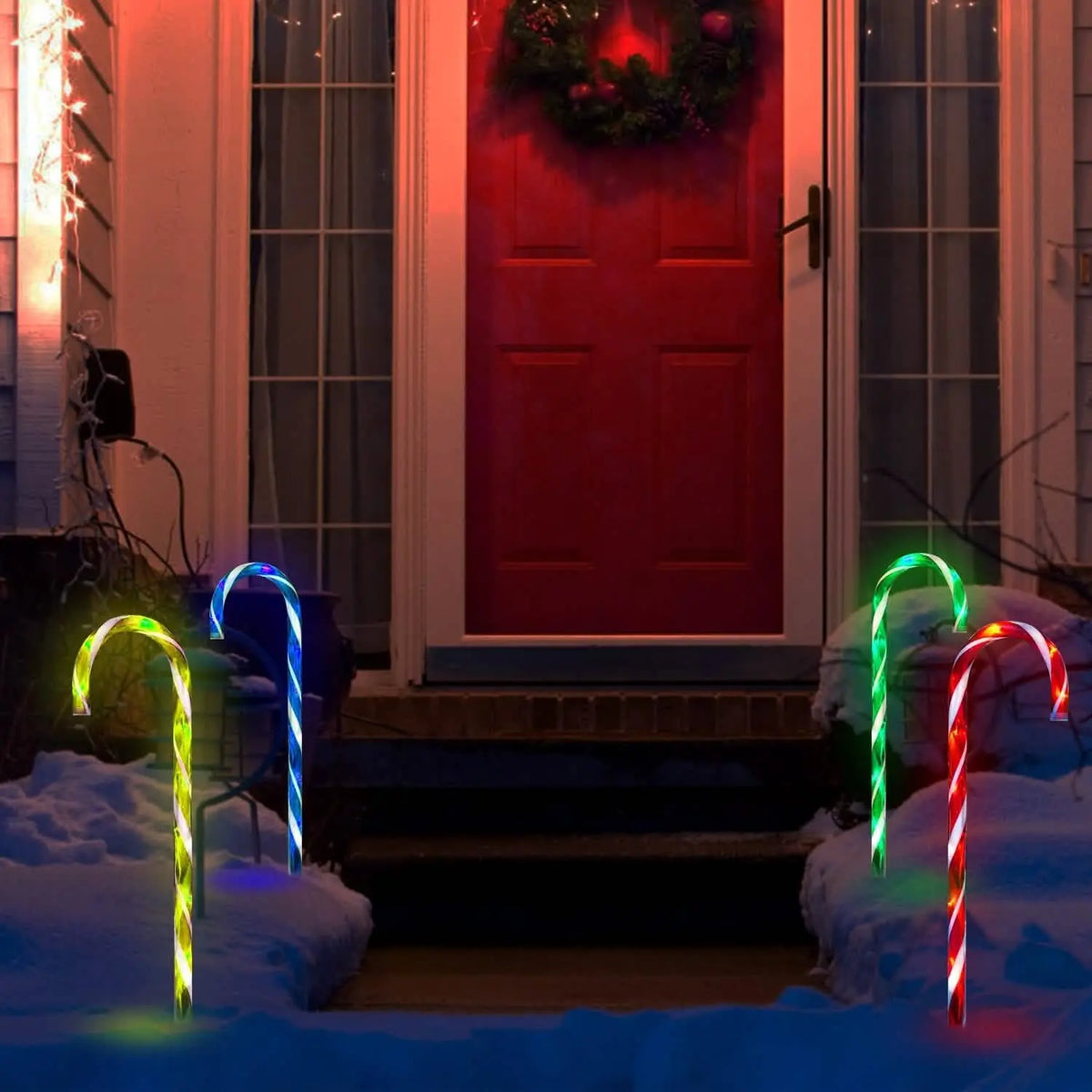 Set of glowing solar candy cane stake lights in multicolor on snowy walkway