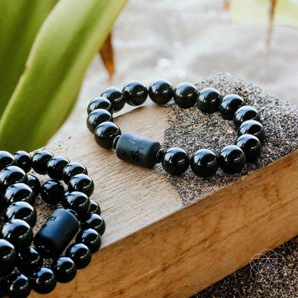 Black obsidian bead bracelet with barrel charm laid on wood surface