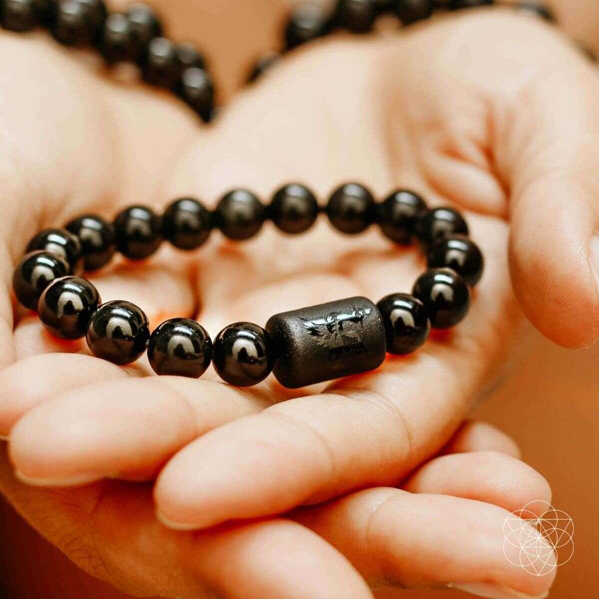 Black obsidian bead bracelet held in hand, featuring a faceted barrel charm