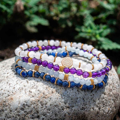 Multi-strand beaded bracelet with white, purple, and blue beads and gold-tone center charm
