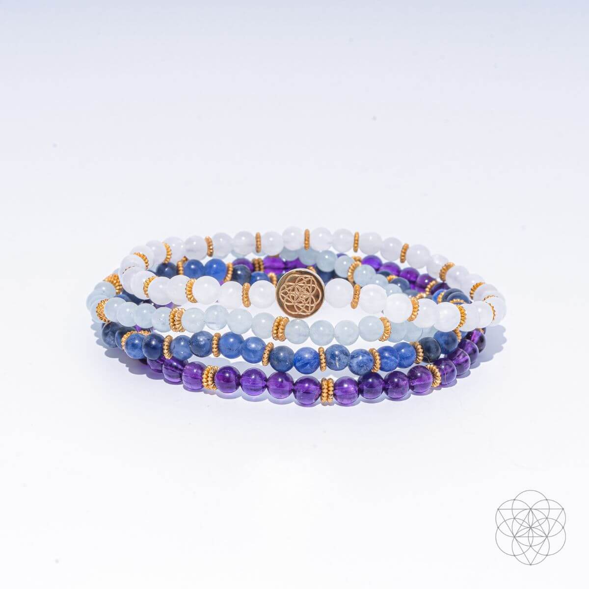 Multi-strand beaded bracelet with white, purple, and blue gemstones and gold-tone charm