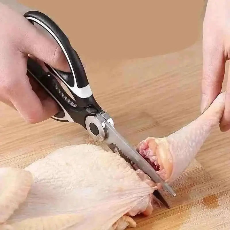 Kitchen scissors with serrated blade cutting raw poultry, black-and-silver handle