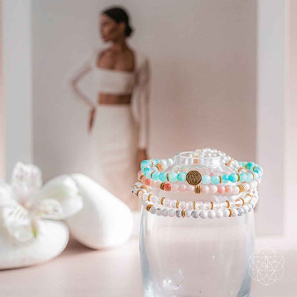 Beaded bracelets in turquoise, white, and pink with gold accents displayed on clear cup