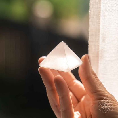 Off-white crystal pyramid held between fingers with sharp triangular tip