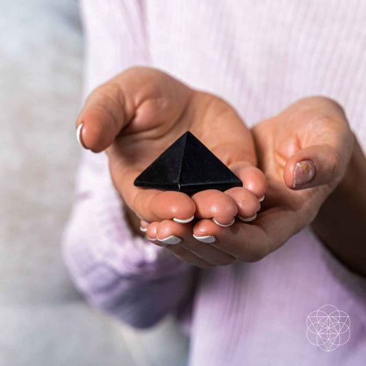 Dark crystal pyramid held in hands with small pyramid size and pointed top