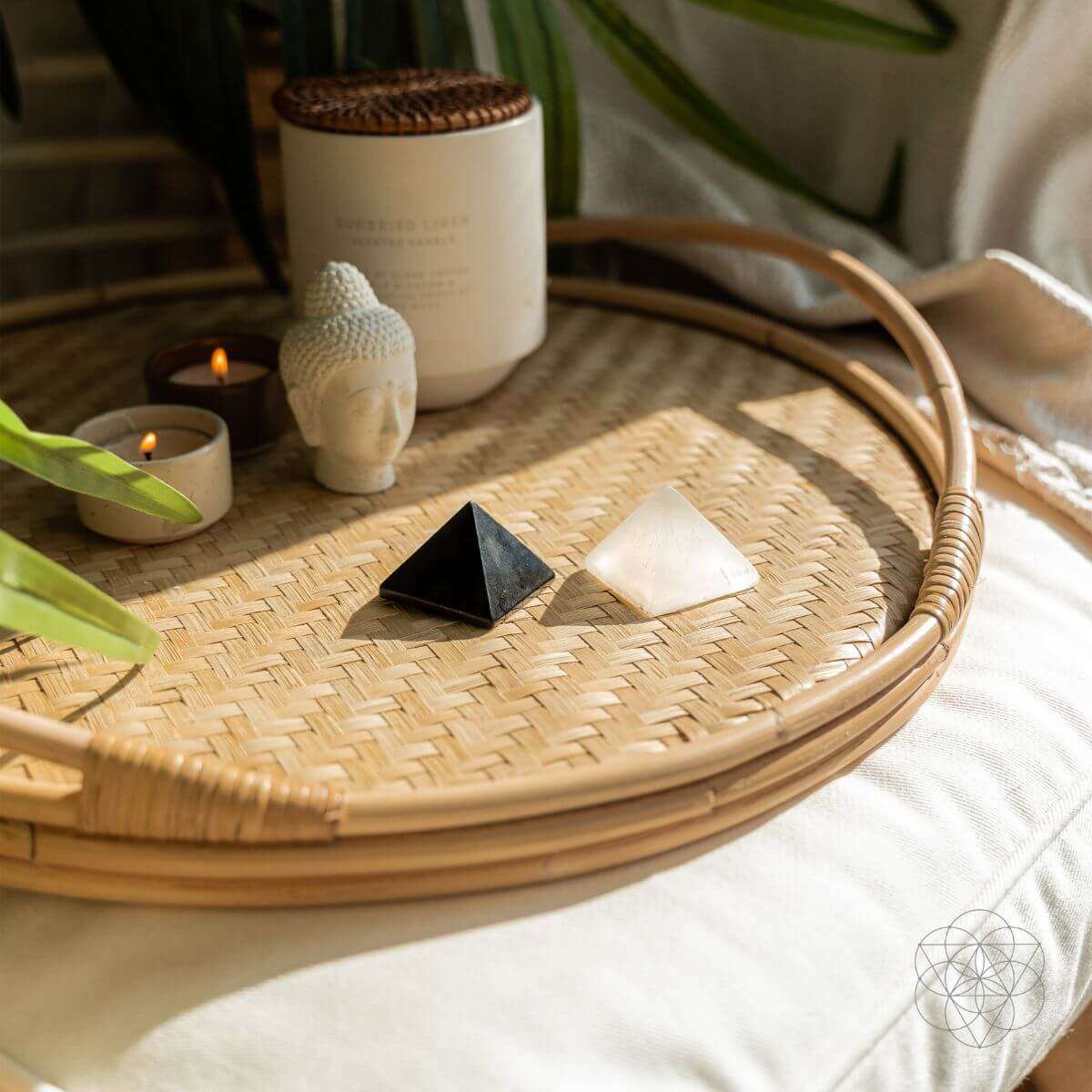 Two small crystal pyramids on a woven tray with candles and decor nearby
