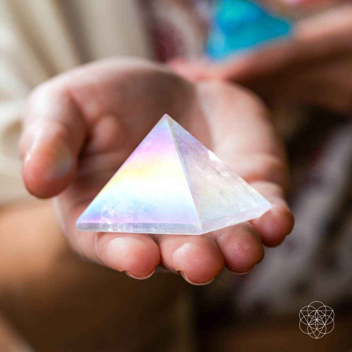 Iridescent angel aura crystal pyramid held in hands with rainbow hues