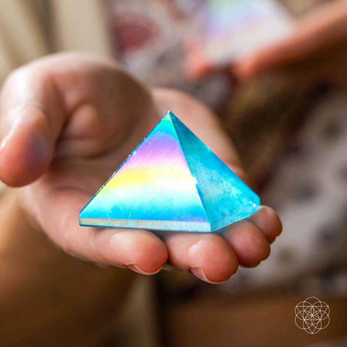 Aqua blue crystal pyramid held in hands with rainbow glow