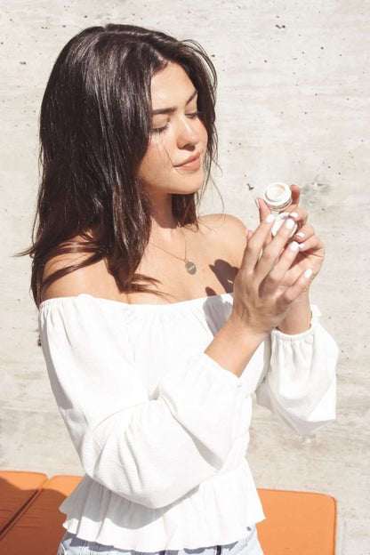 Woman holding a small eye cream jar near her face