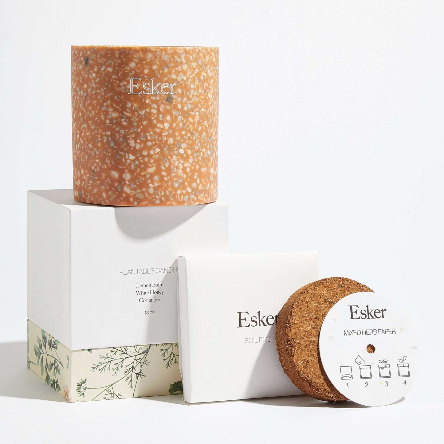 Plantable terracotta candle with Esker label, shown with product boxes and seed disc