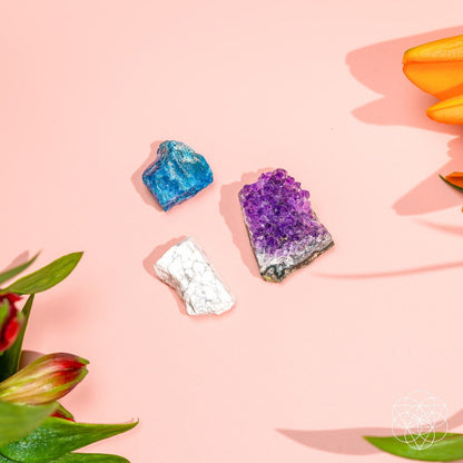 Four small crystal stones on a pink surface: blue, purple, and white pieces