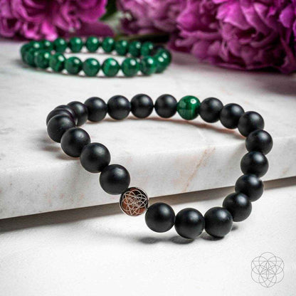 Two beaded bracelets laid flat: matte black beads and green accents with geometric charm