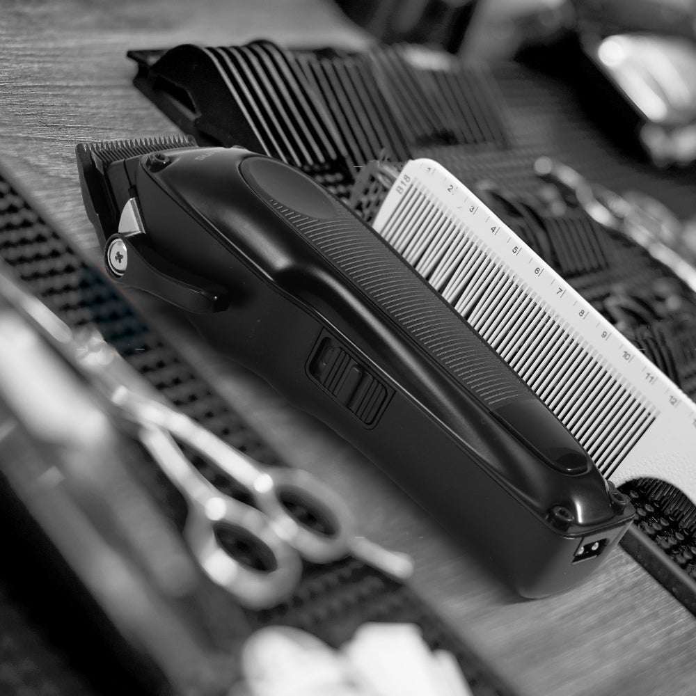 Black hair clipper with side controls and visible comb attachment on table