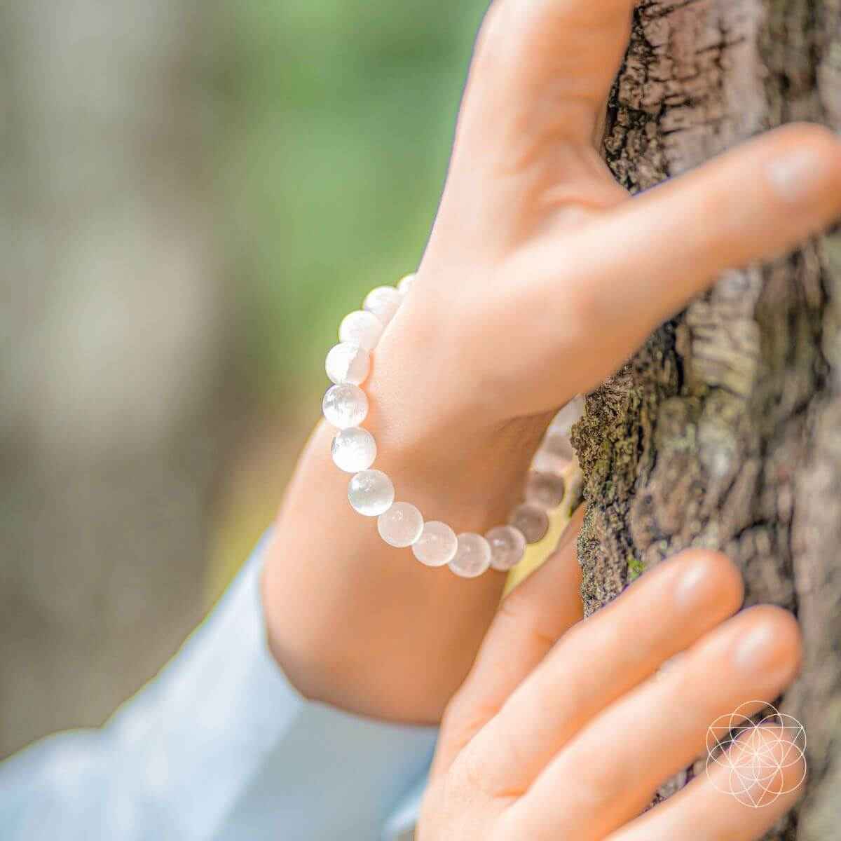 White round-stone beaded bracelet on hand beside tree bark