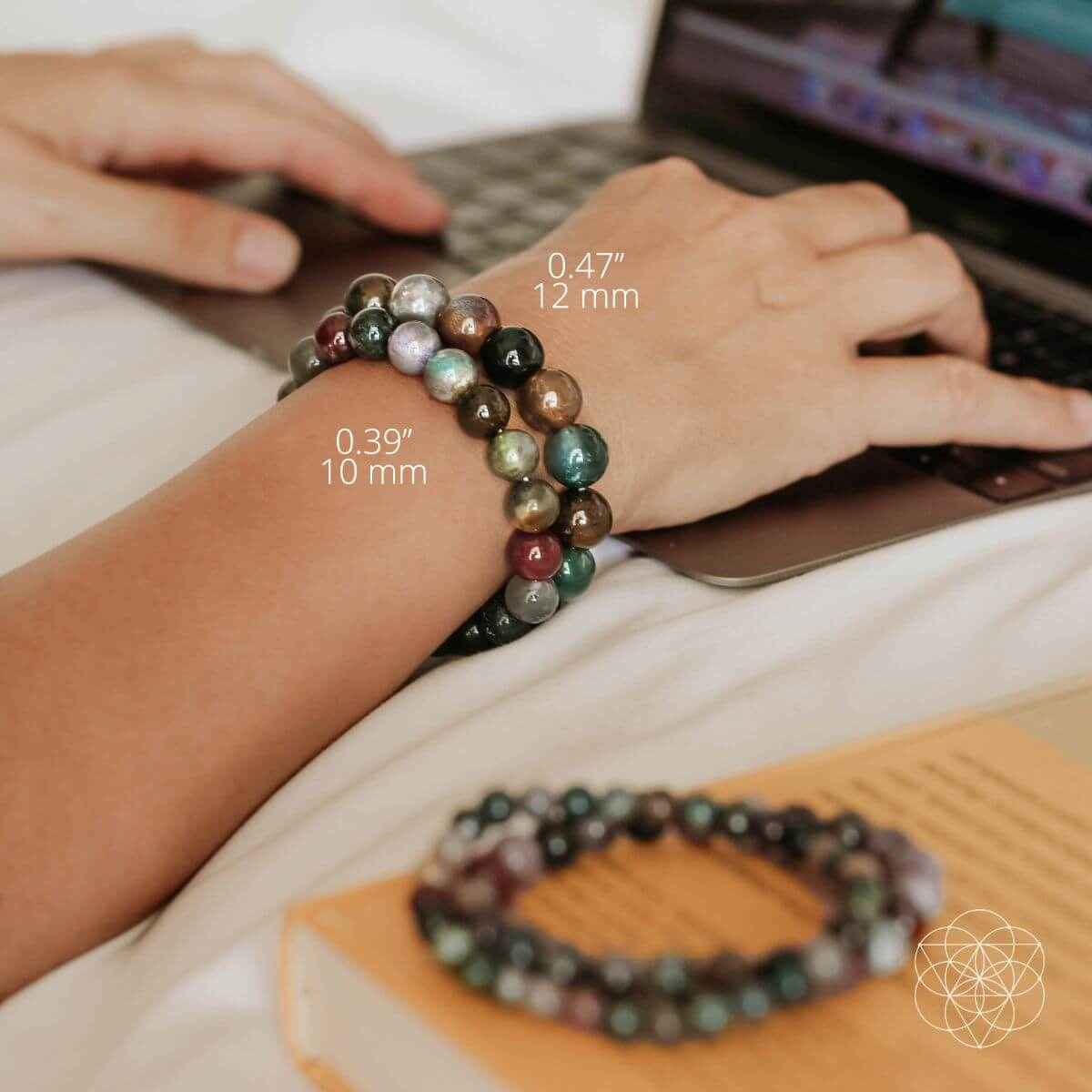 Gemstone bead bracelet on wrist with green, brown, red, and pale round beads