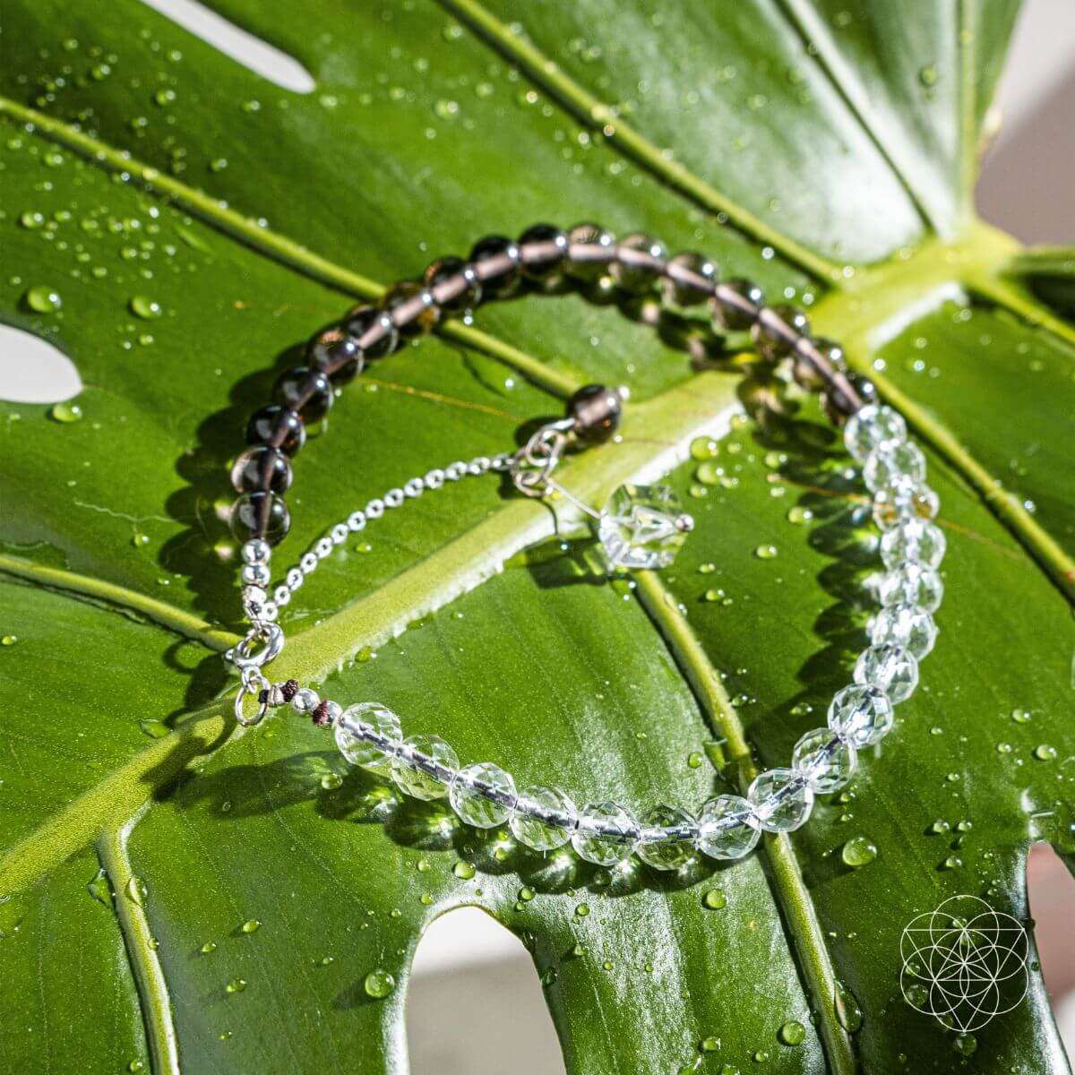 Silver chain anklet with dark beads and clear crystal drops on green leaves