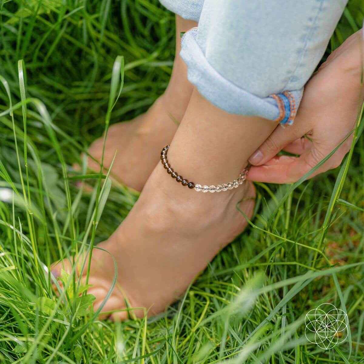 Dark beaded anklet with silver-tone charm, worn on ankle with bare foot