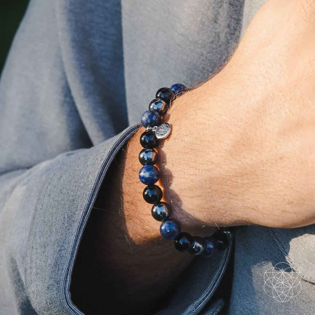 Energy-shield bracelet on wrist with dark blue/black beads and small silver charm