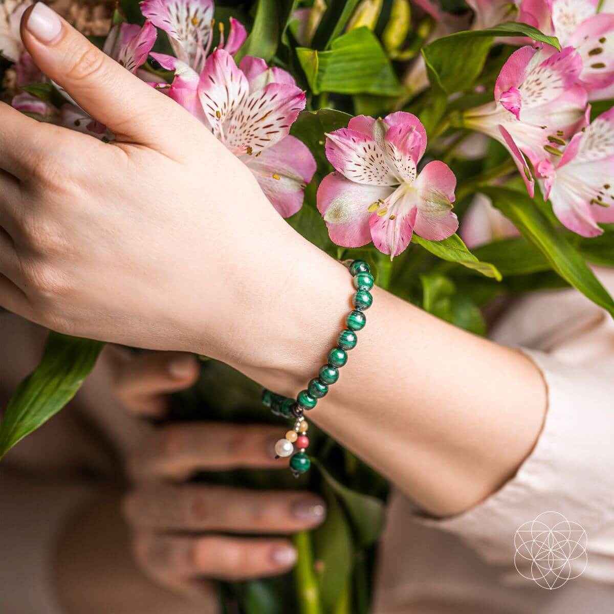 Green beaded bracelet with pink and white charms worn on a wrist