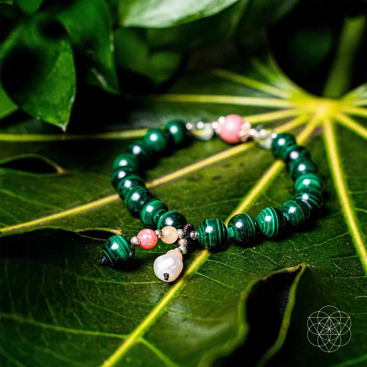 Green beaded bracelet with pink bead, pearl-like drop, and small gold charms