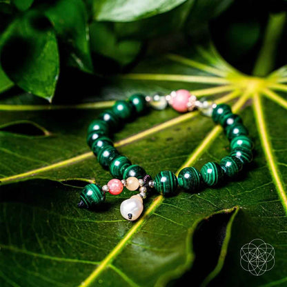 Green beaded bracelet with pink bead, pearl-like drop, and small gold charms