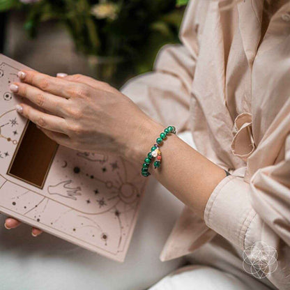 Green beaded bracelet with small charms on wrist, shown with a card