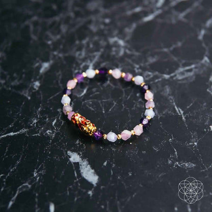 Beaded prosperity bracelet on dark marble, lilac and pink stones with gold charm