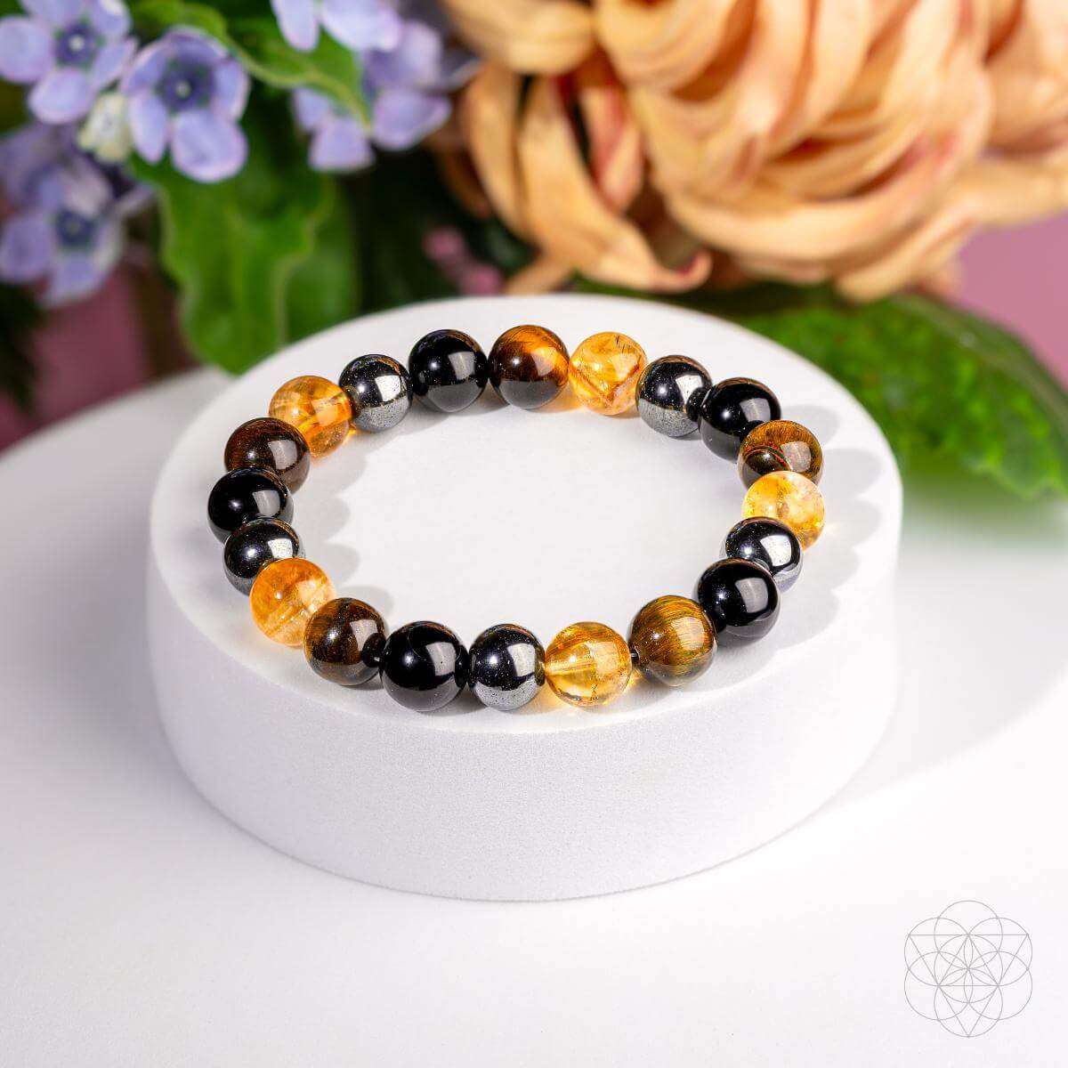 Beaded bracelet with black and amber beads on a white display pedestal.
