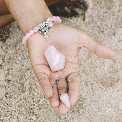 Rose quartz bead bracelet with tree charm and matching raw rose quartz crystal in hand
