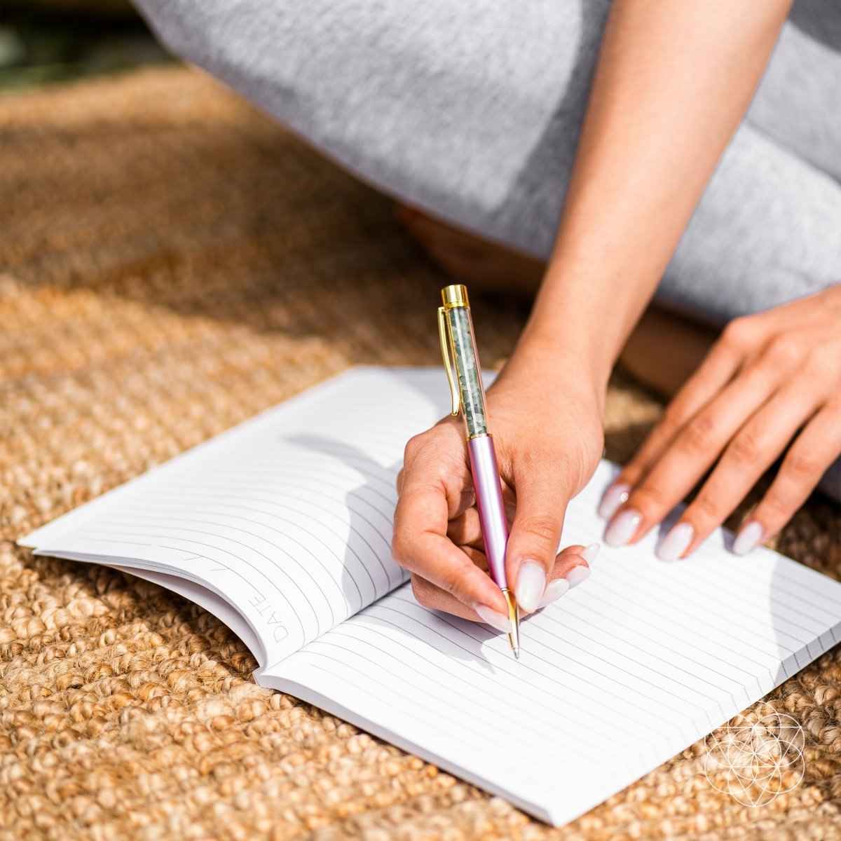 Pink crystal self-cleansing pen writing in an open notebook on a woven surface.