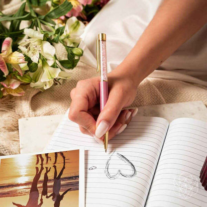 Hand writing with a pink crystal self-cleansing pen on lined notebook paper.