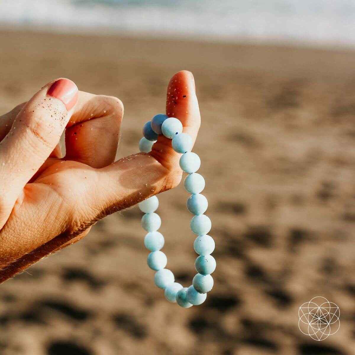 Hand holding sky-blue beaded bracelet with round beads, elastic fit.