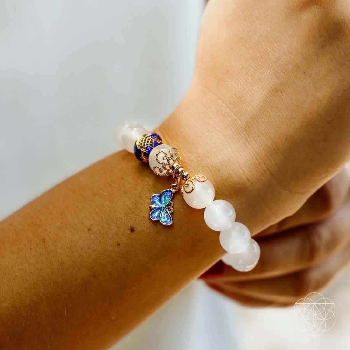 Spiritual growth bracelet on wrist with white beads, blue butterfly charm, and gold accents