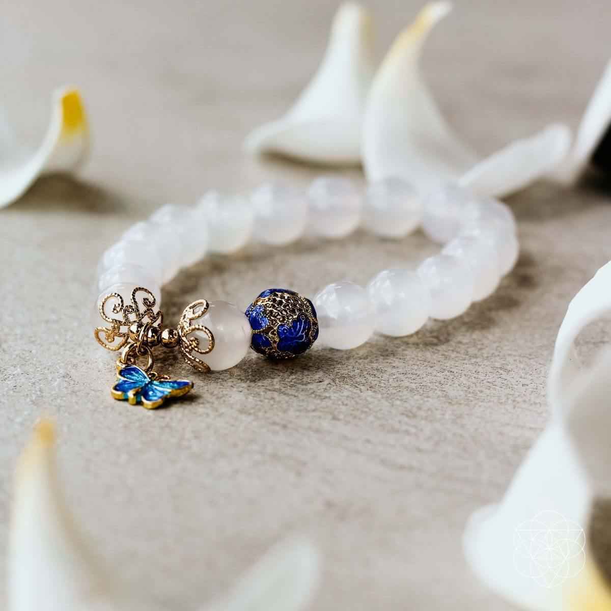 White bead bracelet with blue butterfly charm and gold centerpiece detail laid on light surface