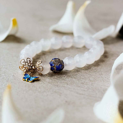 White bead bracelet with blue butterfly charm and gold centerpiece detail laid on light surface