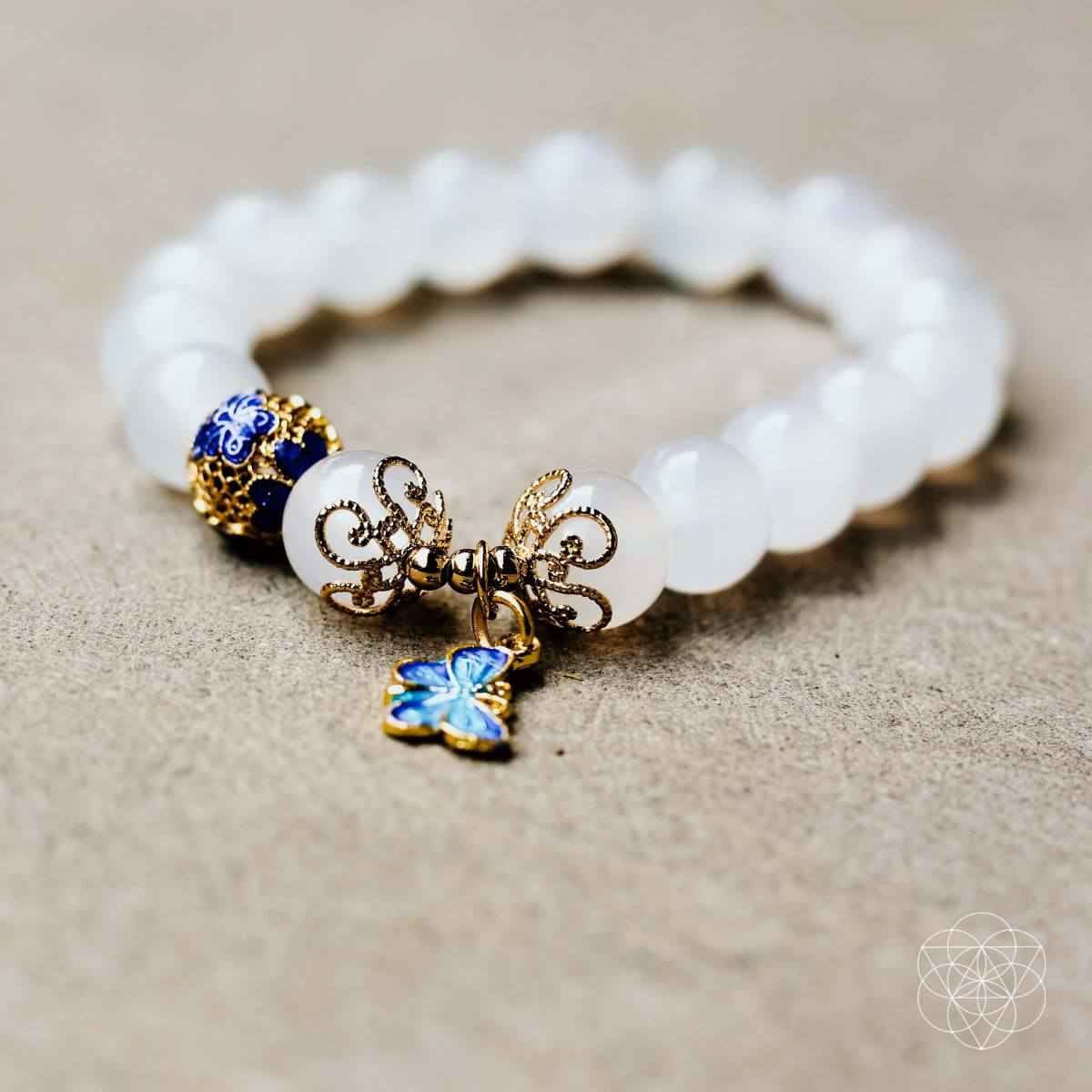 Spiritual growth bracelet featuring white beads and blue butterfly charm with gold filigree links