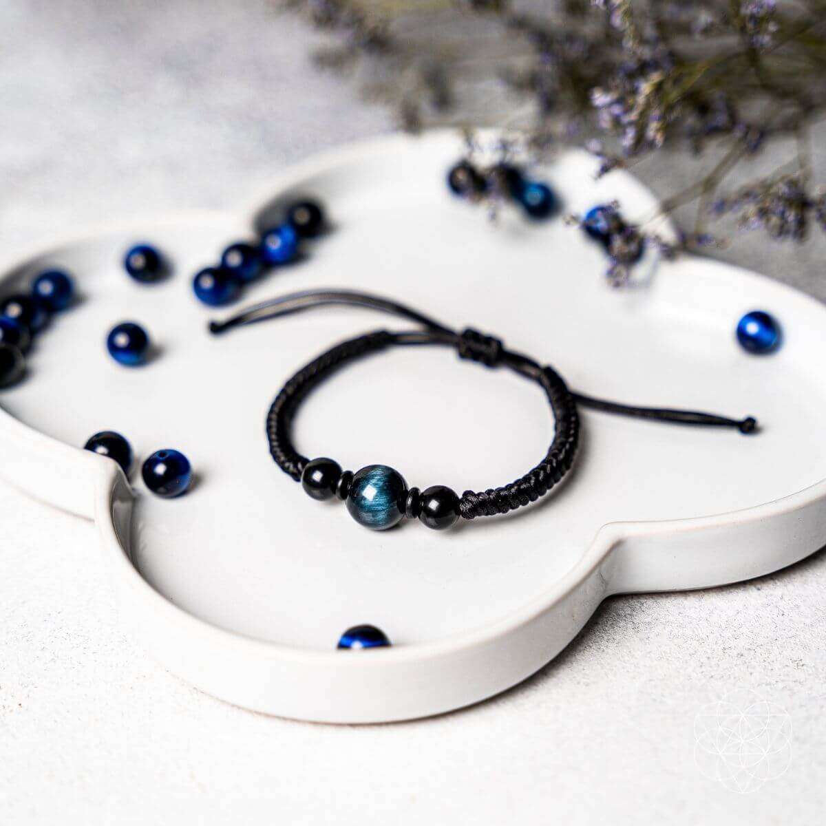 Beaded black cord bracelet with blue beads shown on a white tray
