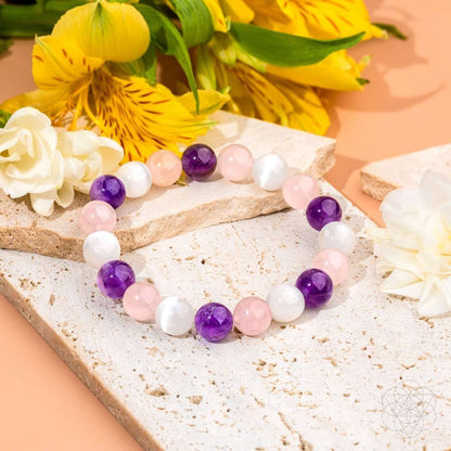 Beaded bracelet with pink, white, and purple stones on a white stone slab with flowers.