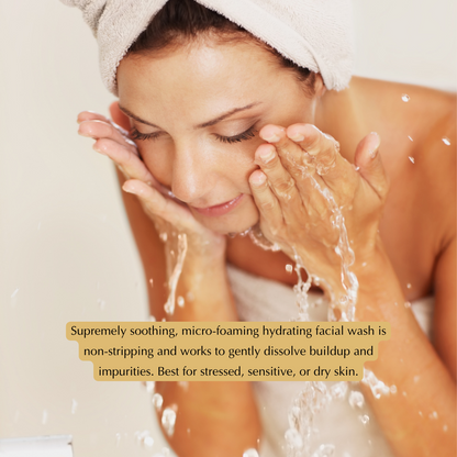 Face being washed with foamy cleanser, towel over hair; lather on cheeks and hands