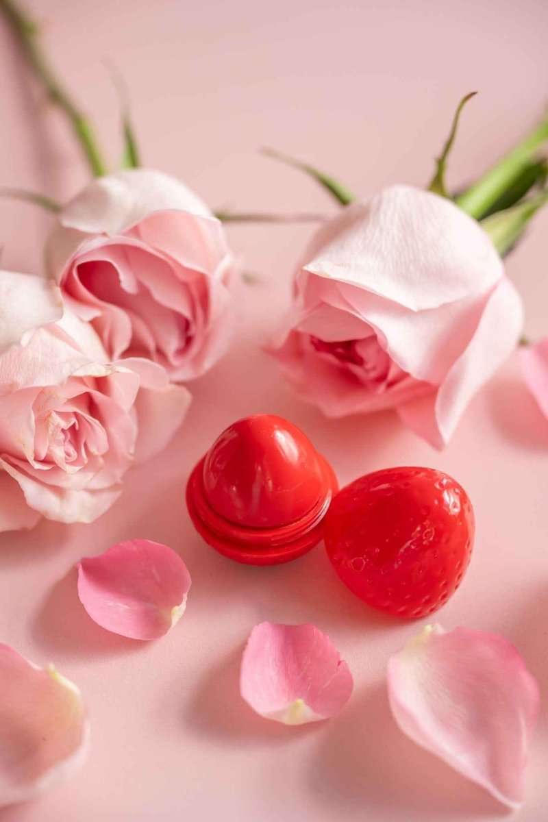 Red lip butter balm dome and open cap with surrounding pink rose petals