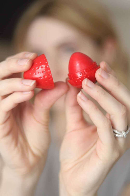 Hands applying red strawberry-shaped lip butter to lips.