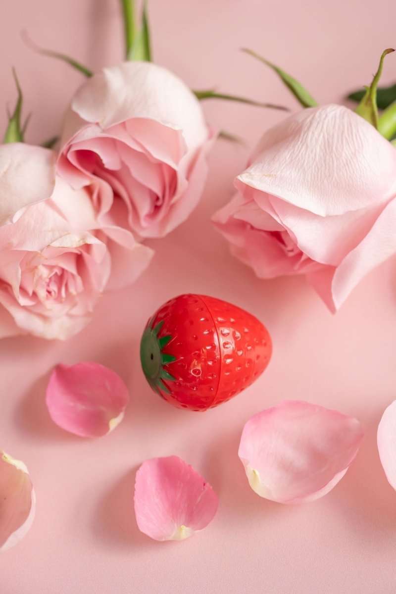 Red strawberry-shaped lip butter with green leaf detail, capped.