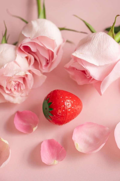 Red strawberry-shaped lip butter with green leaf detail, capped.