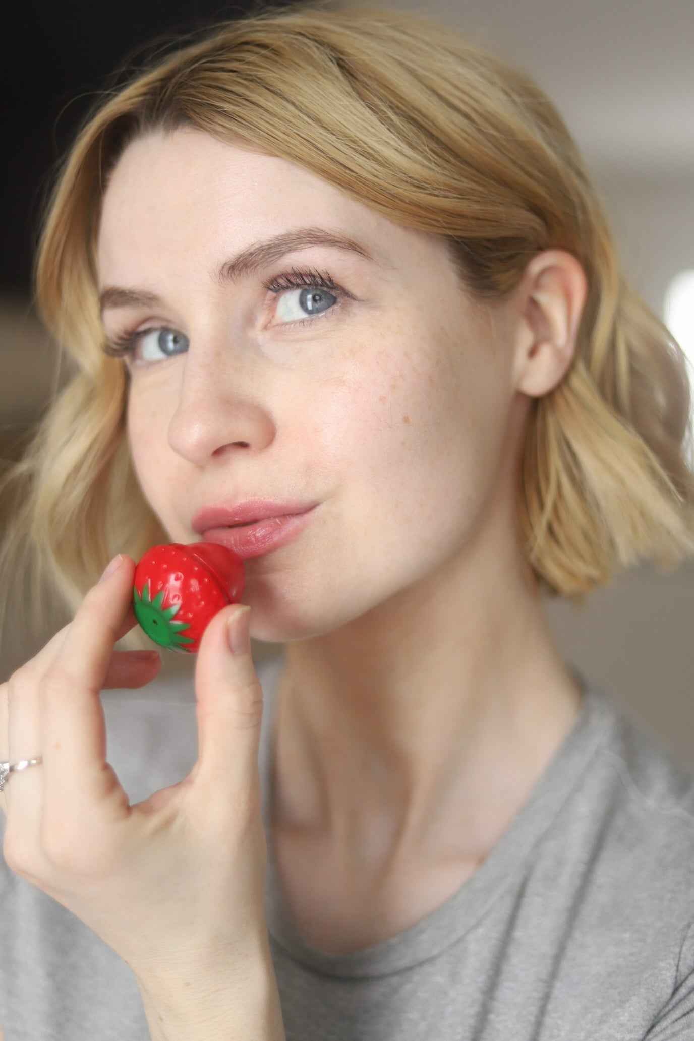 Strawberry-red lip butter balm container with green leaf topper on a fingertip